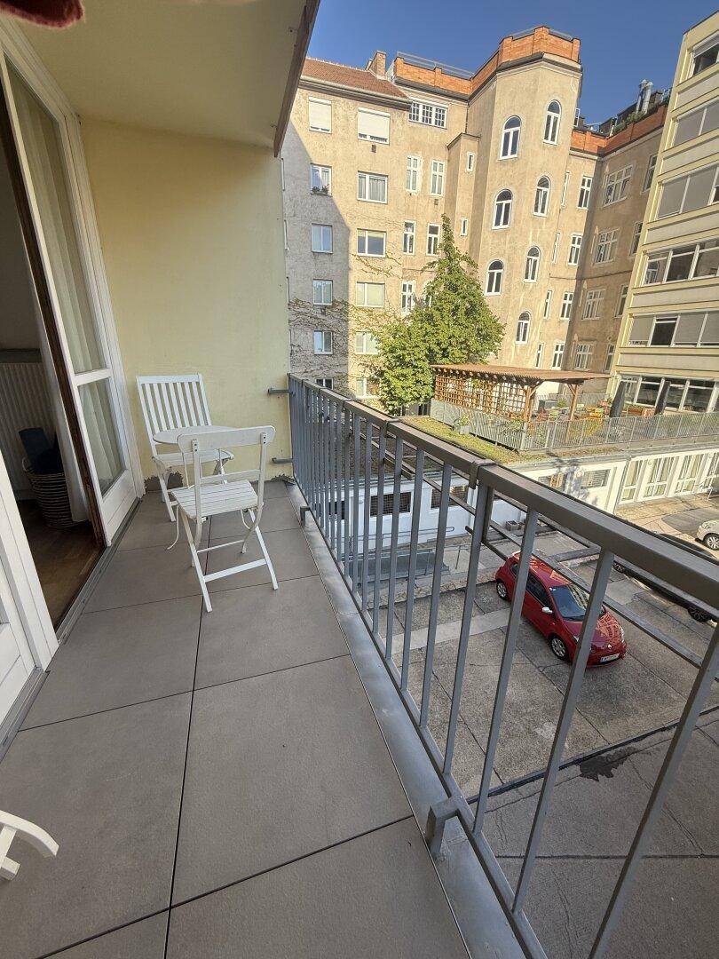 Kleiner Balkon mit Sitzgelegenheiten und Blick auf den Innenhof und umliegende Gebäude.