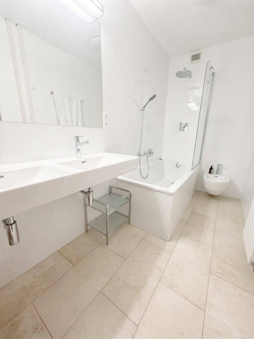 Helles, modernes Badezimmer mit Doppelwaschbecken, Badewanne mit Dusche und Bidet.