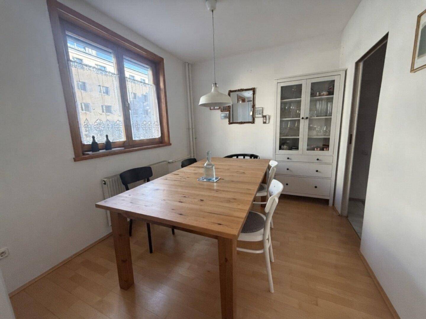 Gemütlicher Essbereich mit großem Holztisch, Stühlen und einem weißen Vitrinenschrank.