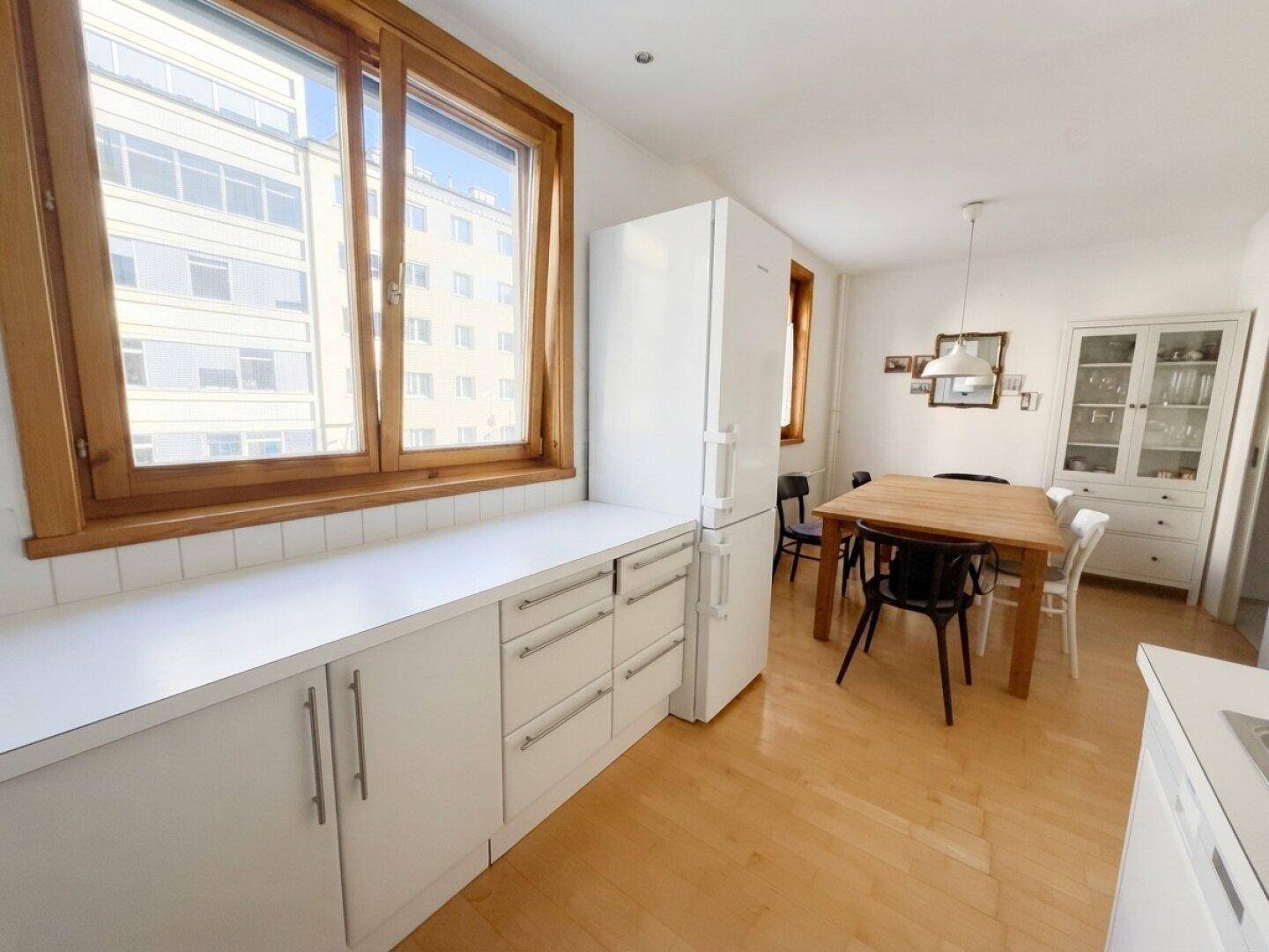 Funktionale Küche mit weißen Schränken, großem Fenster und Essbereich mit Holztisch.