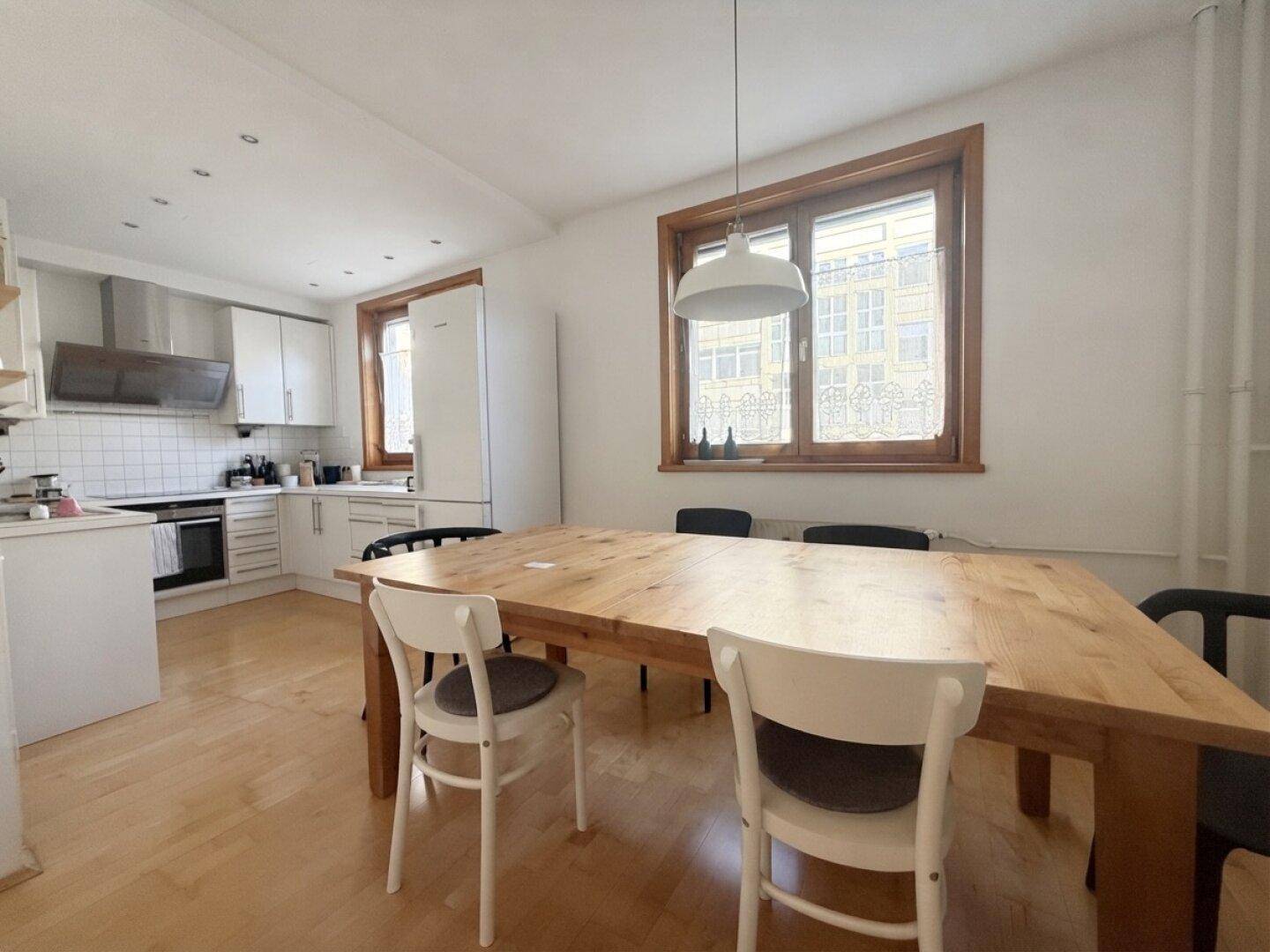 Geräumige Wohnküche mit großem Holztisch und moderner Küchenzeile im Hintergrund.