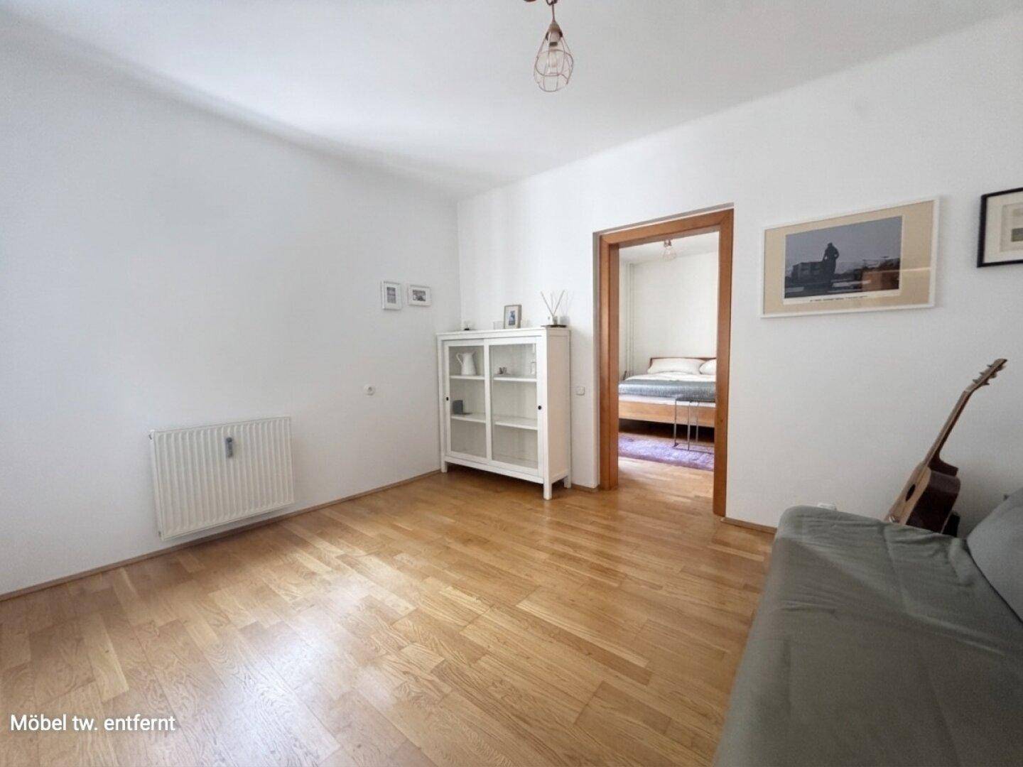Wohnzimmer mit Sofa und weißem Schrank, mit direktem Zugang zu einem Schlafzimmer.