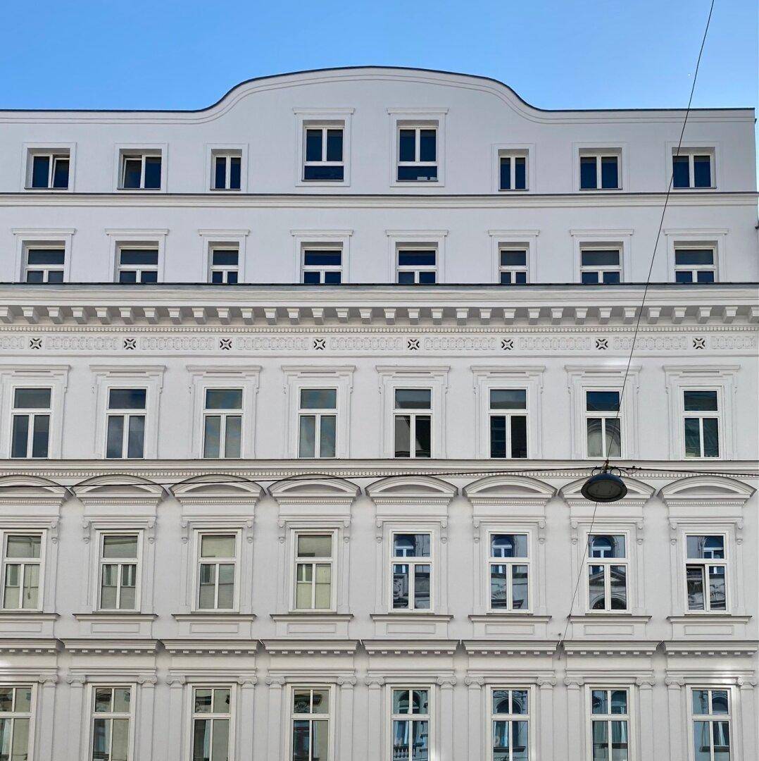 Klassische weiße Fassade eines Altbaus mit zahlreichen Fenstern und dekorativen architektonischen Elementen.