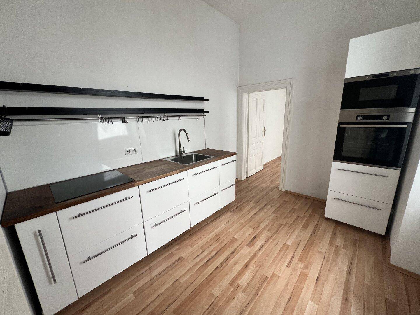 Moderne Einbauküche mit weißen Schränken, Holz-Arbeitsplatte und integrierten Geräten.