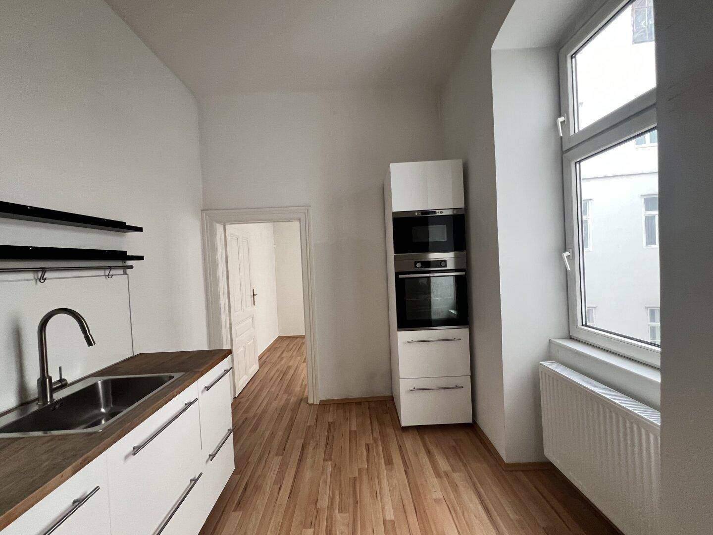 Helle Küche mit modernen weißen Unterschränken, Holz-Arbeitsplatte und Fensterblick.