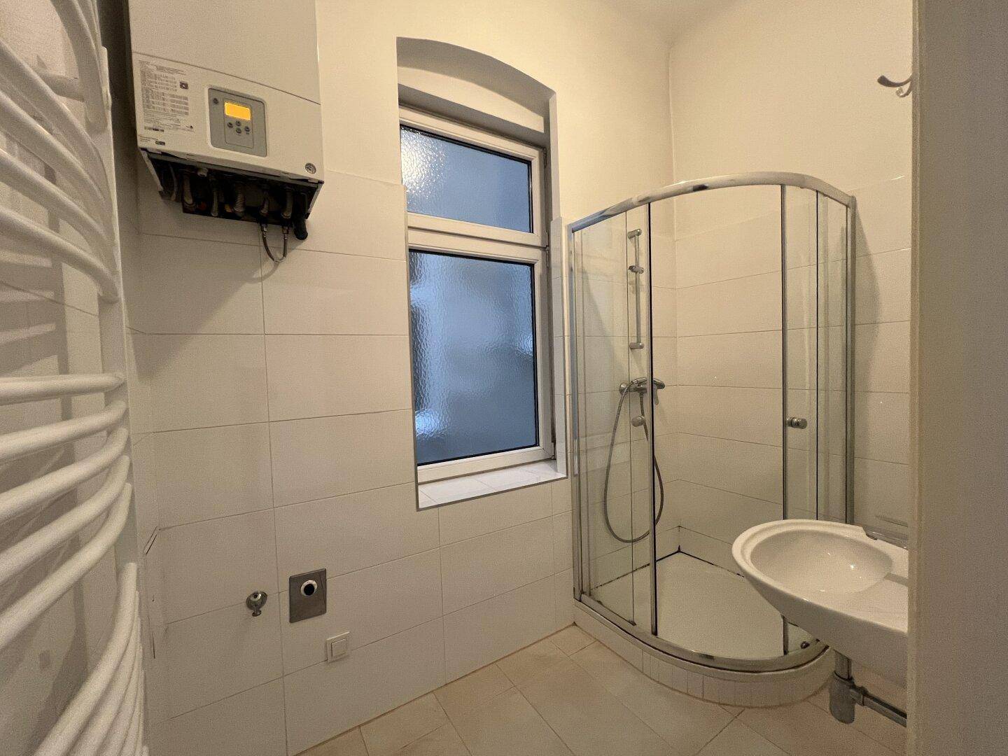 Modernes Badezimmer mit Duschkabine, Waschbecken und Heizkörper, hell gefliest.