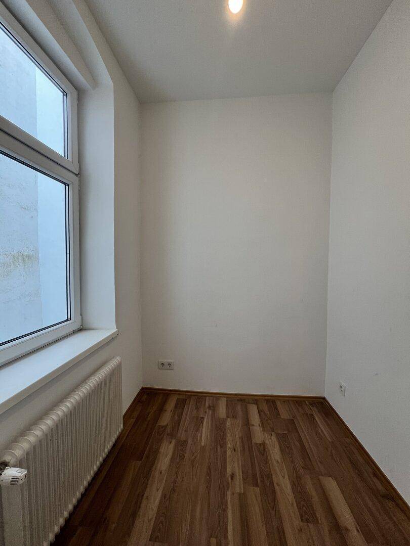 Helles, leeres Zimmer mit Parkettboden und einem großen Fenster, bereit zur individuellen Gestaltung.