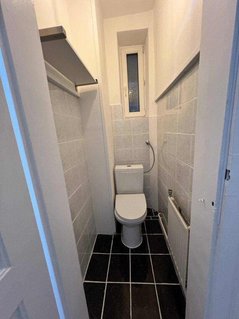 Schmale Gästetoilette mit WC, Fliesenboden und einem kleinen Fenster für Belüftung.
