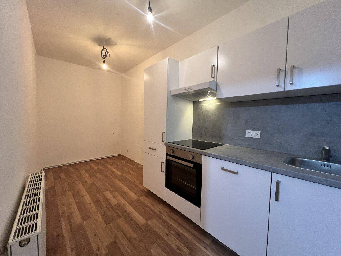Funktionale Küchenzeile mit weißen Schränken, integriertem Backofen und Laminatboden.