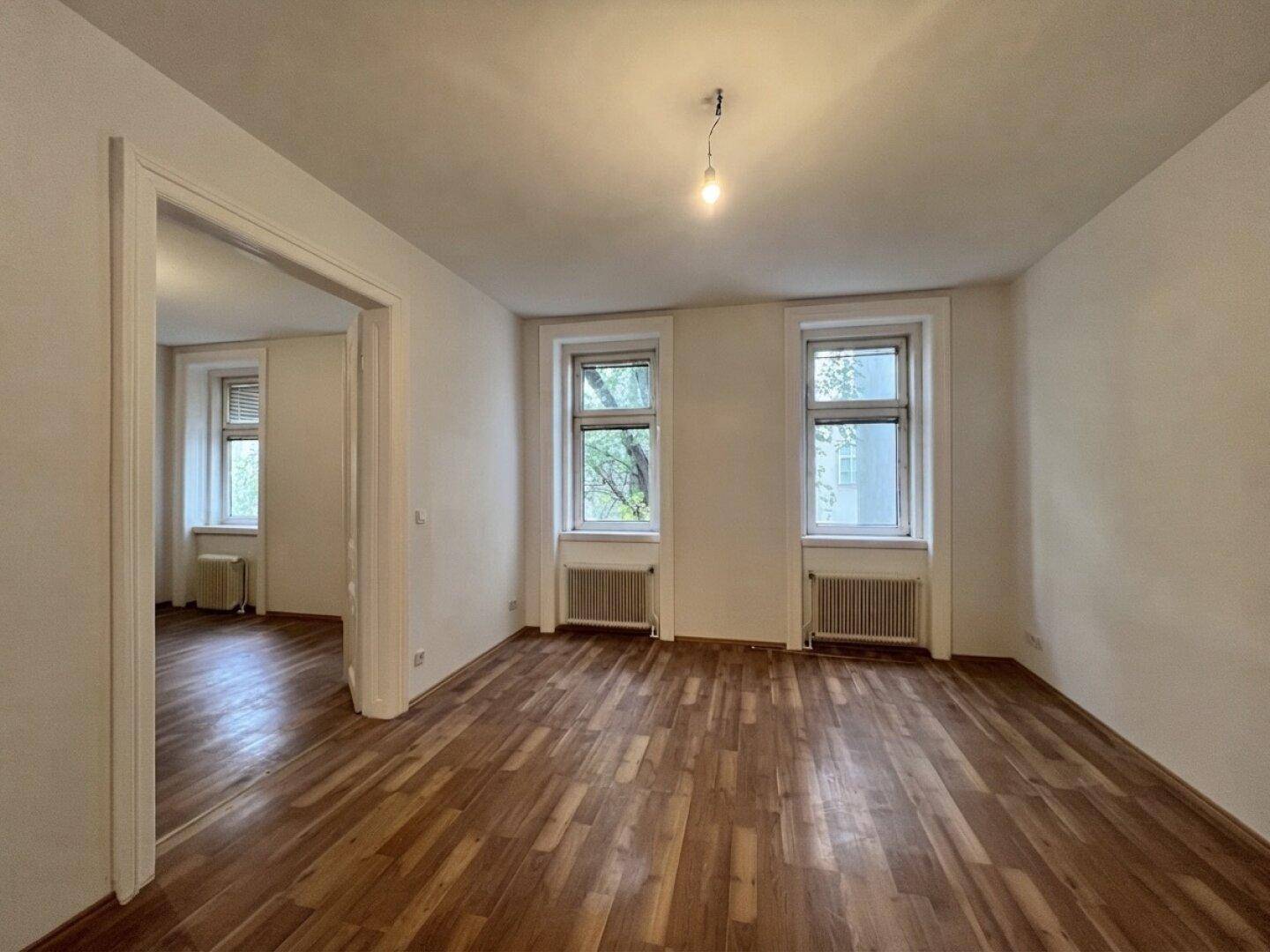 Geräumiges Zimmer mit Holzboden und Blick ins Grüne, ideal als Wohn- oder Schlafzimmer.
