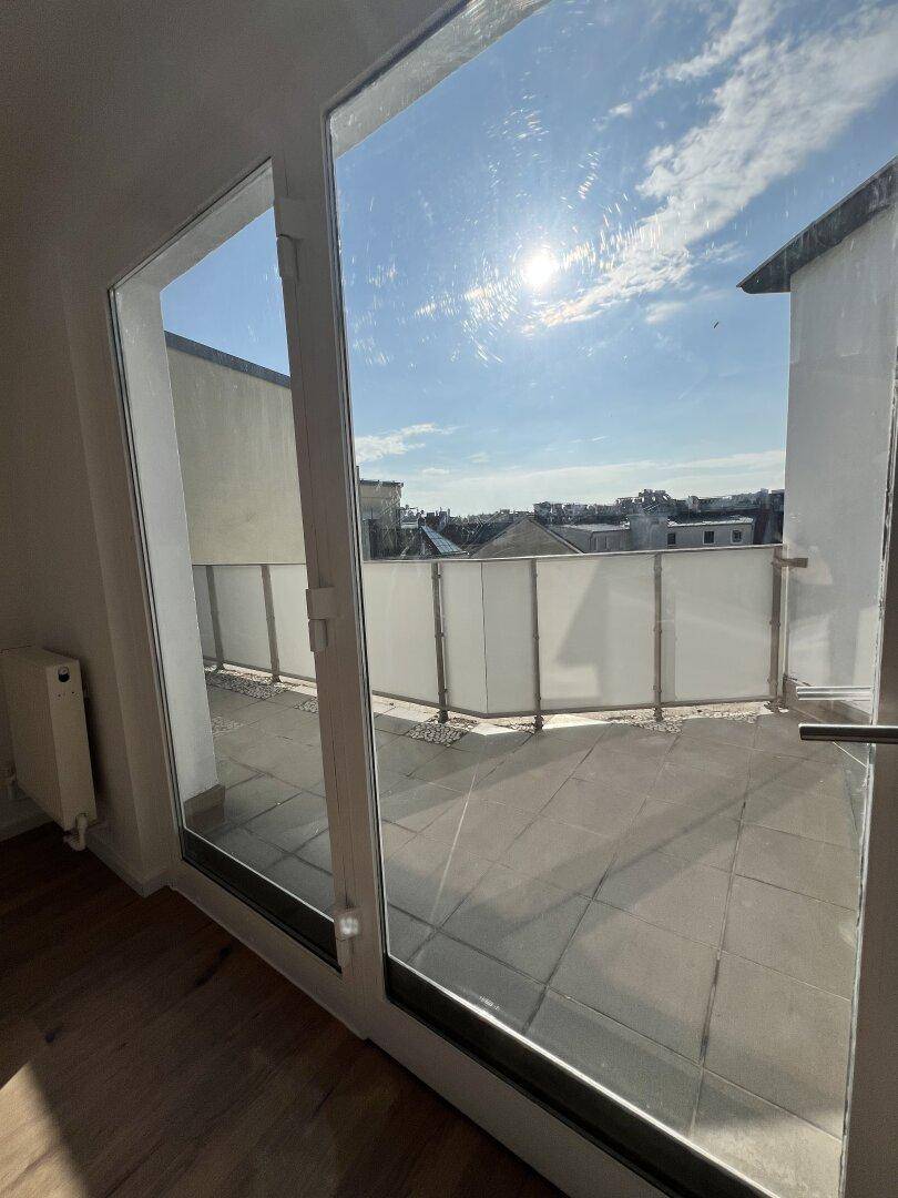 Sonniger Außenbereich mit Fliesenboden und Blick auf die umliegenden Gebäude.