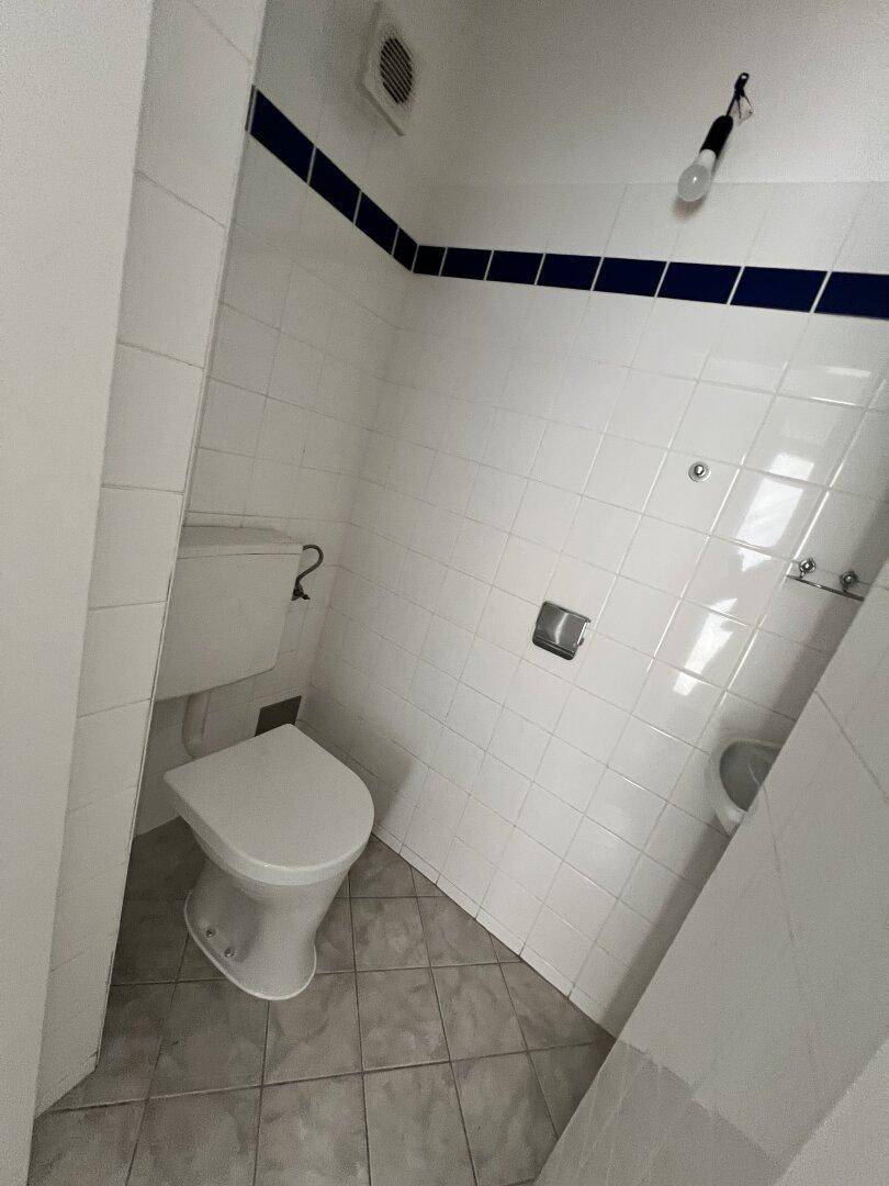 Kleines WC mit weißen Fliesen und blauer Bordüre, funktional und sauber.