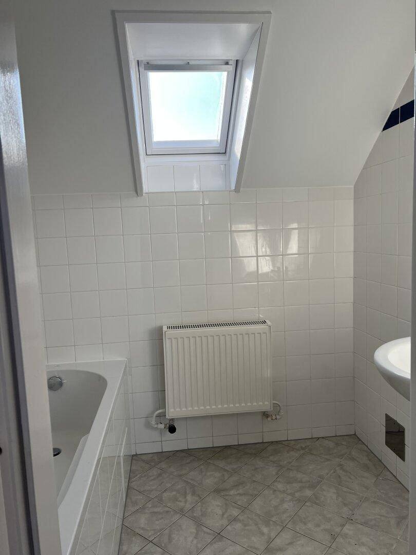 Helles Badezimmer mit Badewanne, Waschbecken und Dachfenster, komplett gefliest.