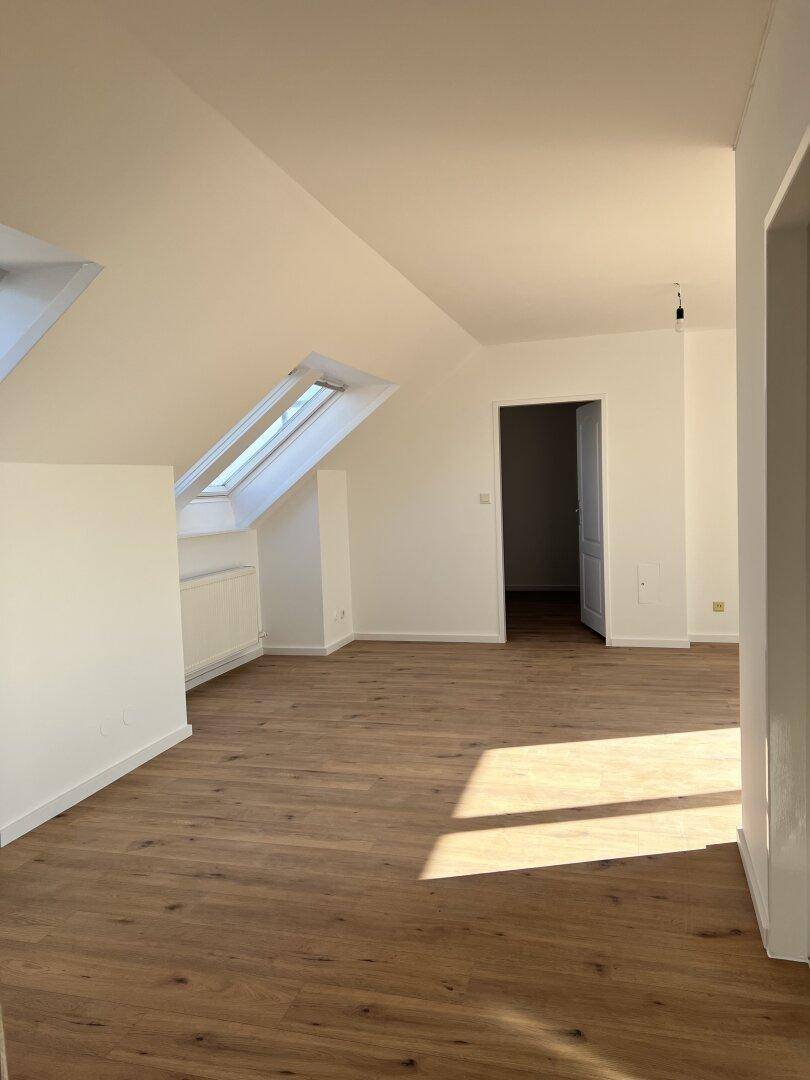 Lichtdurchfluteter Dachraum mit Holzboden und schrägen Wänden, bereit zur individuellen Gestaltung.
