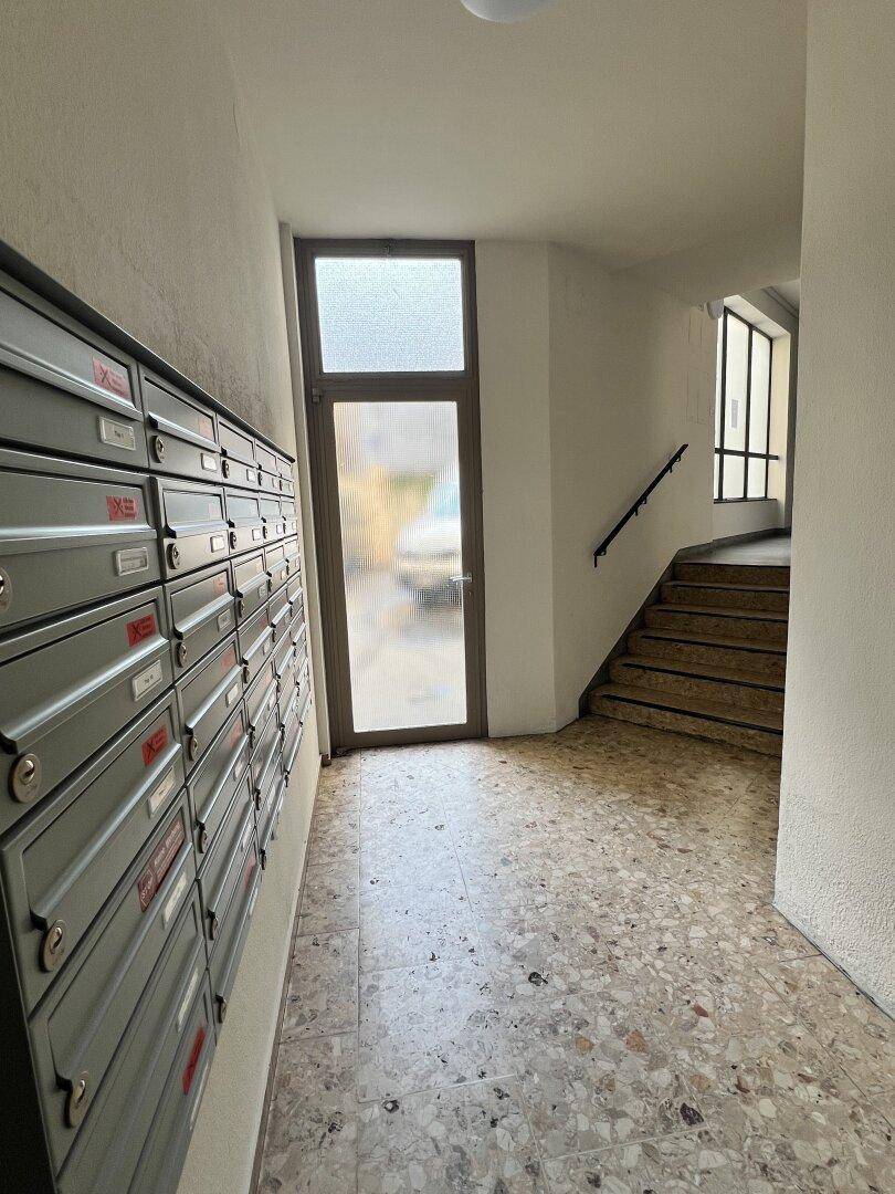 Eingangsbereich eines Mehrfamilienhauses mit Briefkästen und Treppenaufgang.