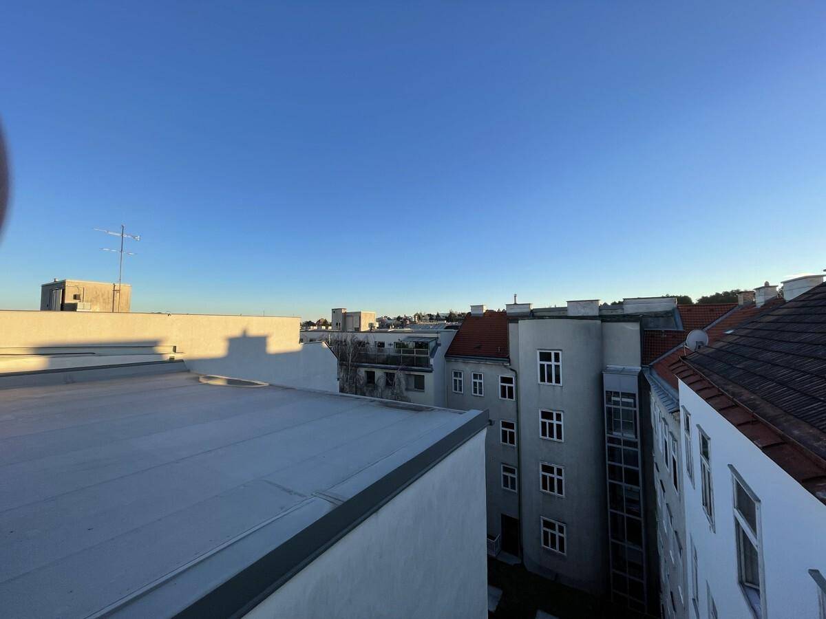 Weitläufiger Blick über die Dächer der Stadt mit verschiedenen Gebäudetypen unter blauem Himmel.