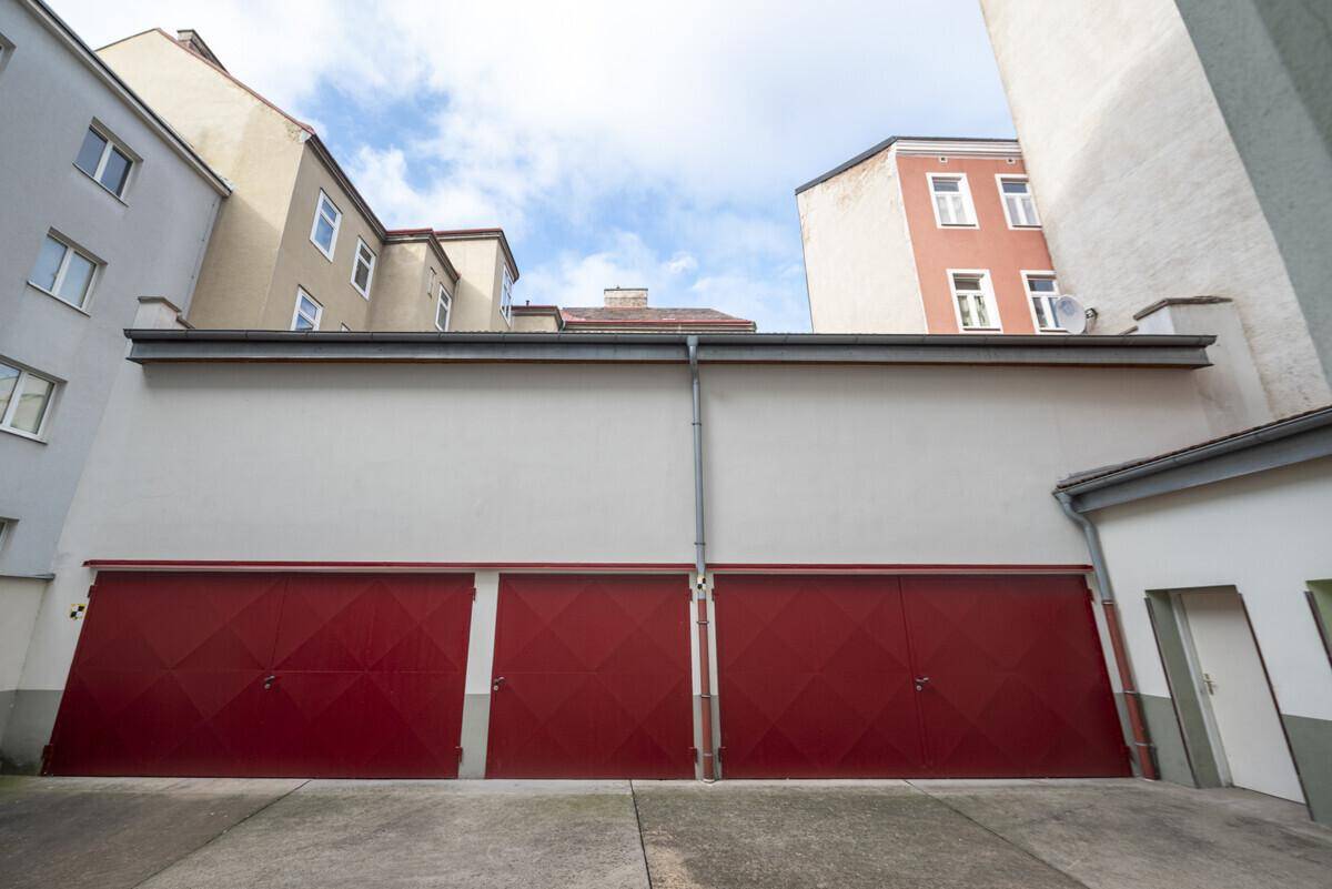 Rote Garagentore in einem Hinterhof, umgeben von weiteren Gebäuden.