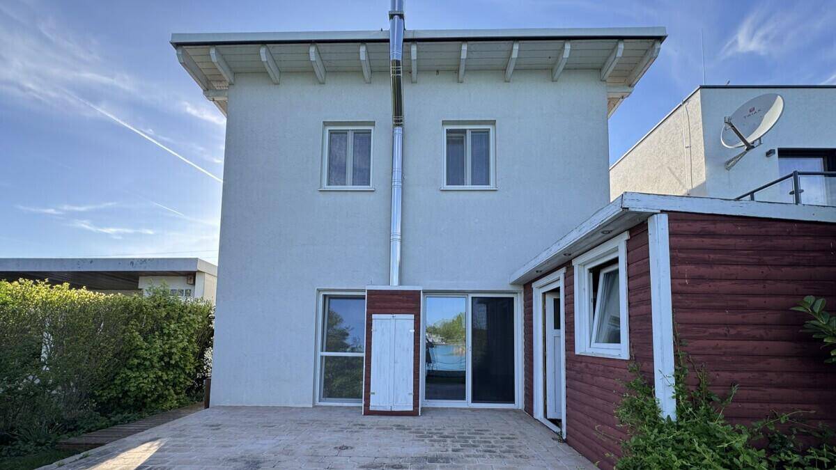 Rückansicht des Hauses mit gepflastertem Bereich, kleinem Schuppen und Blick auf den See.