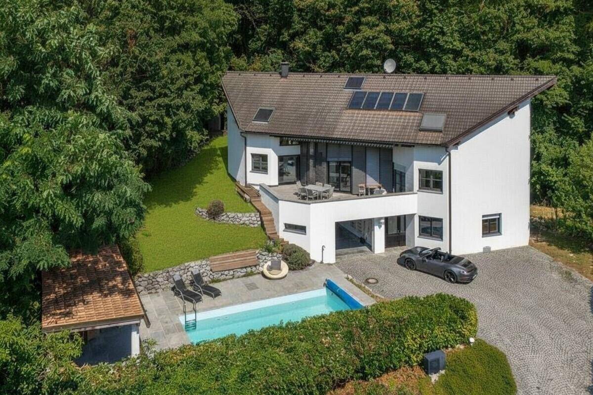 Modernes Haus mit Pool, großer Terrasse und Solaranlage, umgeben von viel Grün.