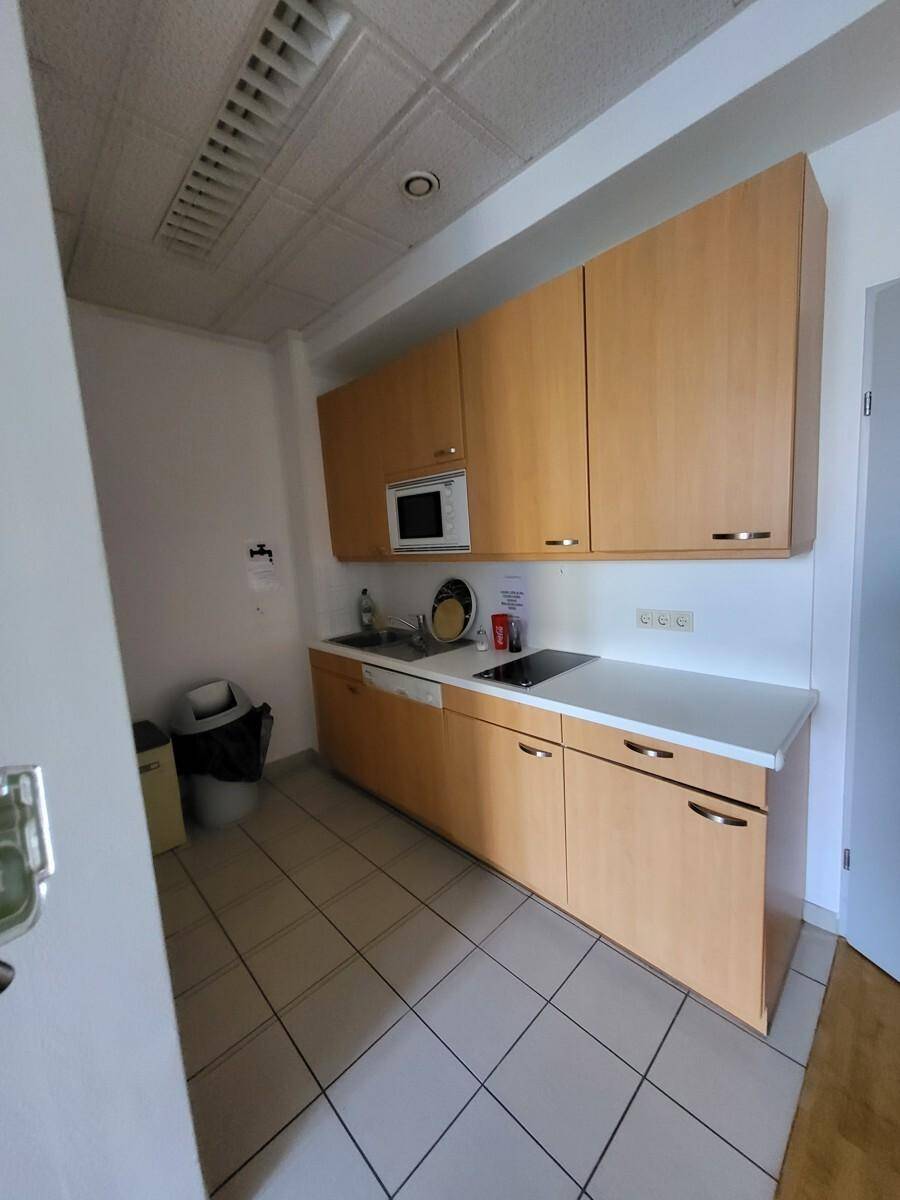 Kleine Teeküche mit Holzschränken, Spüle, Mikrowelle und Induktionskochfeld, praktisch und funktional.