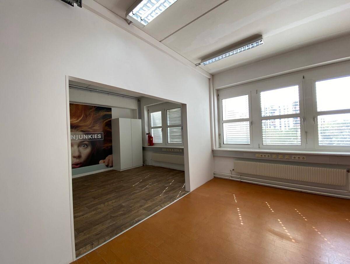 Heller Büroraum mit Fliesenboden und Zugang zu einem weiteren Bereich mit Wandgrafik.