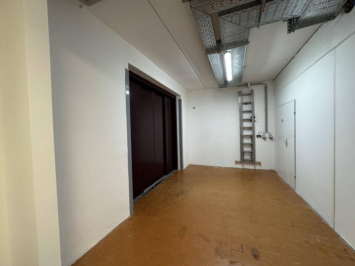 Innenraum mit Lastenaufzug, sichtbaren Kabeltrassen und einer Leiter an der Wand.