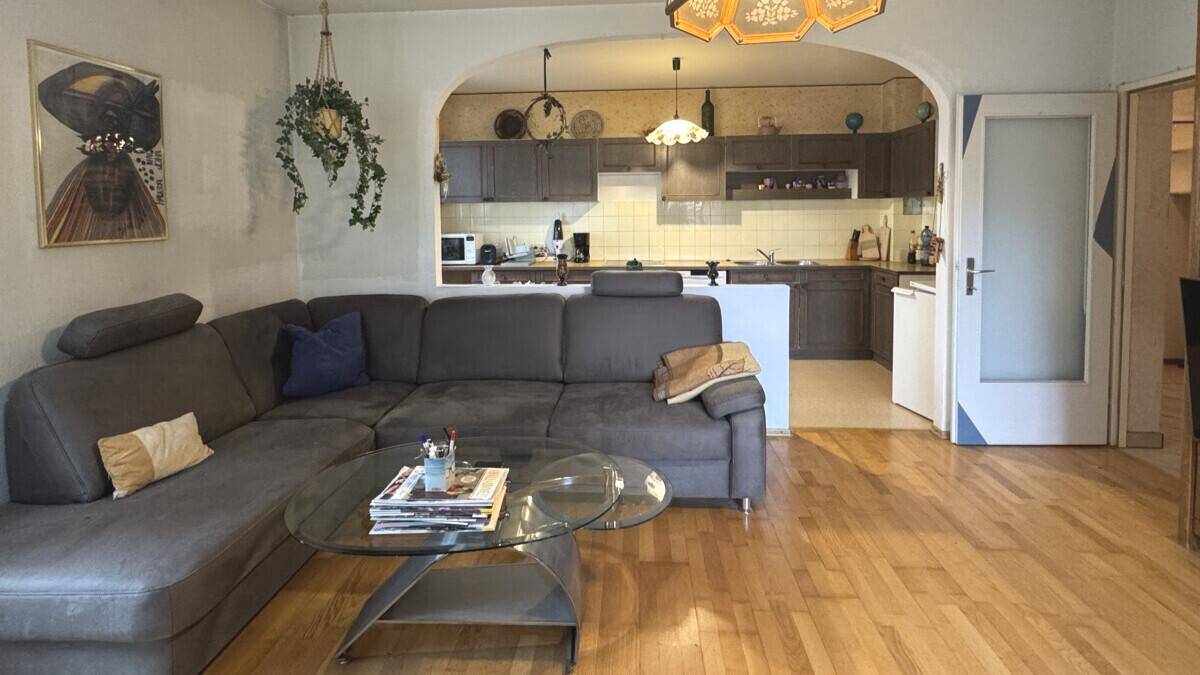 Gemütliches Wohnzimmer mit grauem Ecksofa und offenem Übergang zur Küche, ausgestattet mit Holzfußboden.