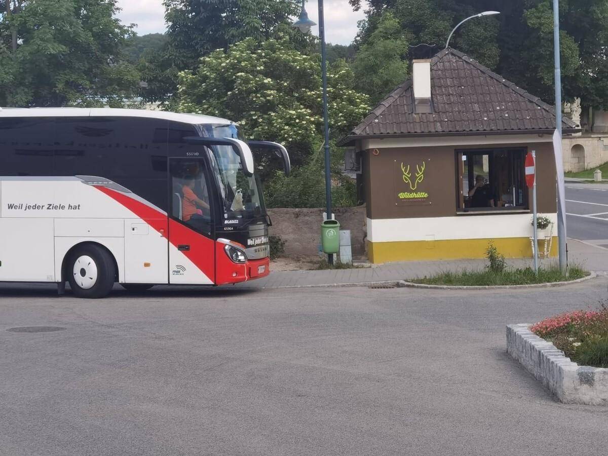Kleines Gebäude an einer Straße, während ein Reisebus vorbeifährt, unter hellem Tageslicht und blauem Himmel.