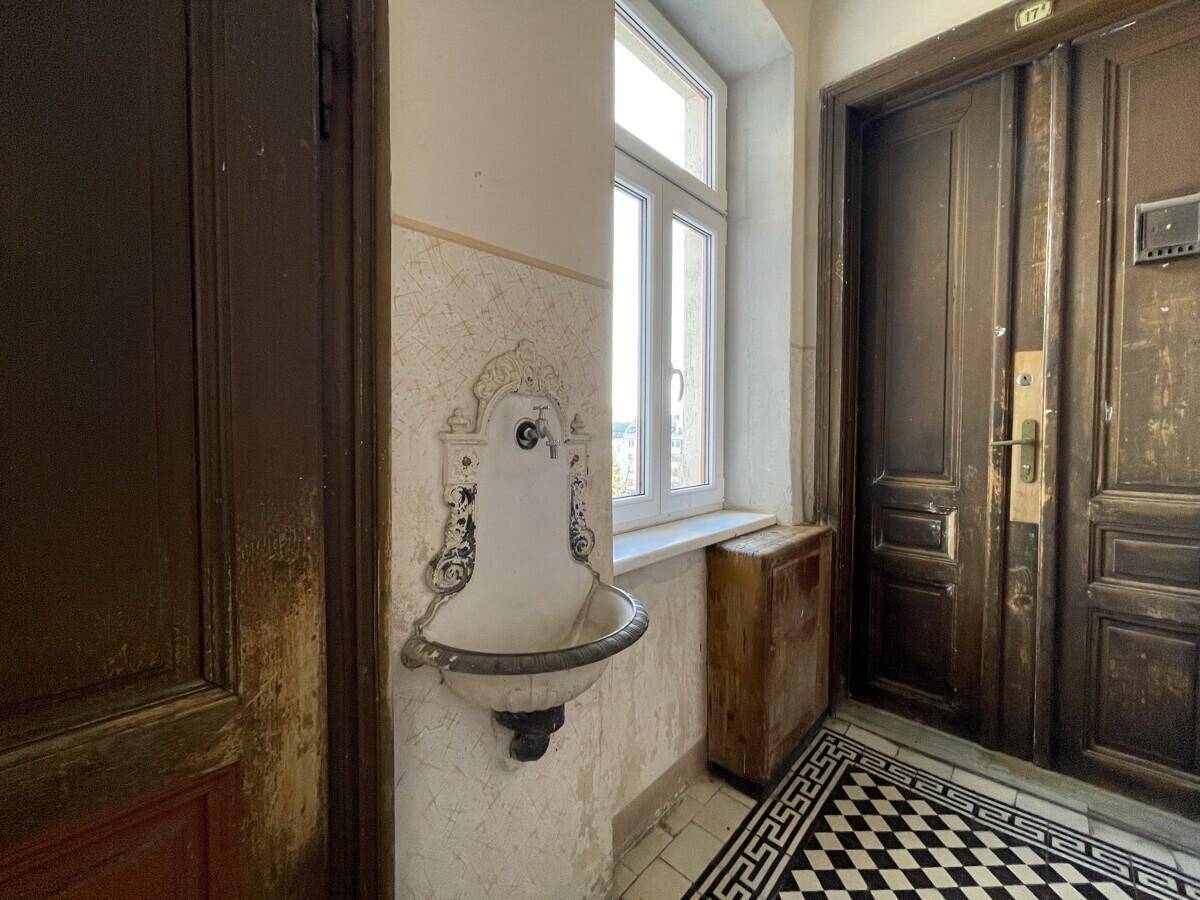 Historisches Waschbecken im Flur eines Altbaus mit gemusterten Fliesen und Fenster.