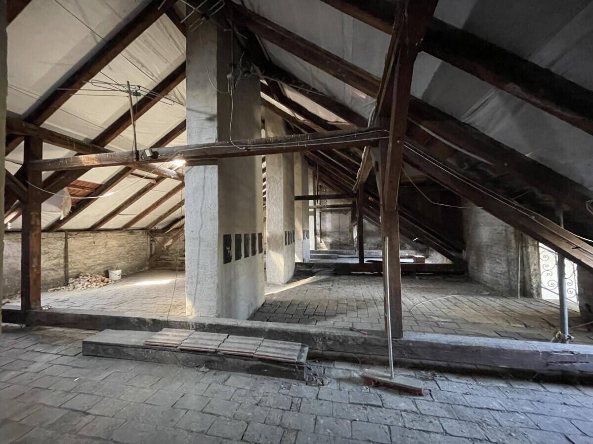 Geräumiger, unausgebauter Dachboden mit sichtbaren Holzbalken und Ziegelboden.