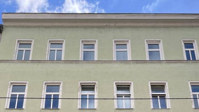 Klassische Gebäudefassade mit hellgrüner Putzfassade und weißen Fenstern.