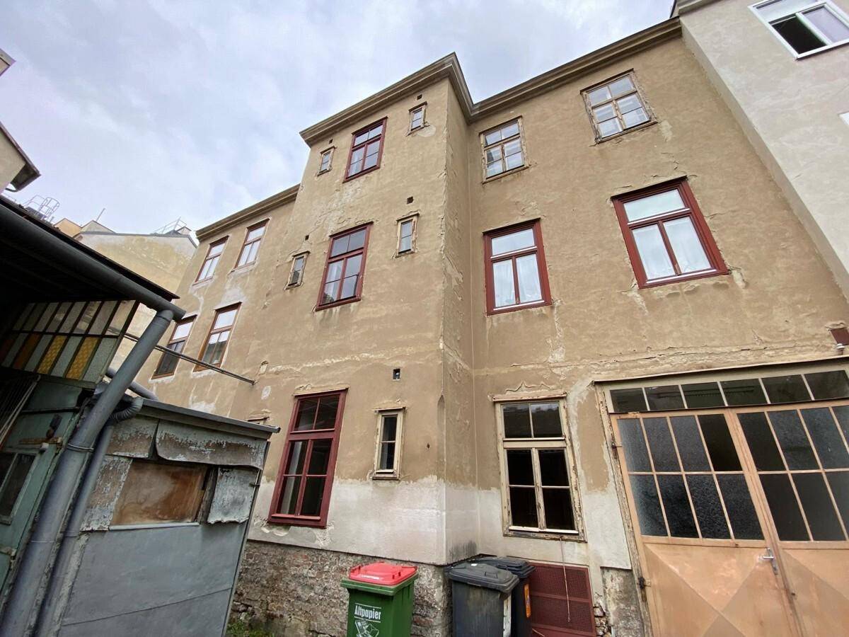 Fassade eines älteren Gebäudes mit roten Fensterrahmen und sichtbaren Abnutzungsspuren, die Renovierungsbedarf andeuten.