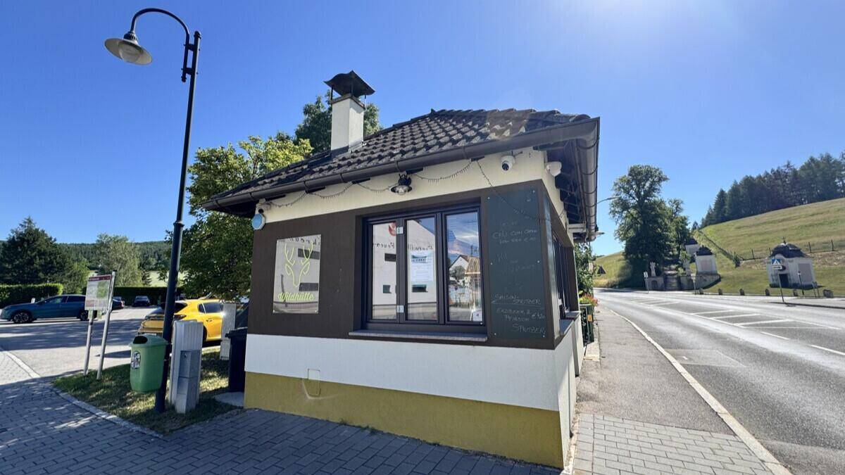 Das kleine Gebäude an einer Straße mit Blick auf eine hügelige Landschaft und weitere Gebäude.