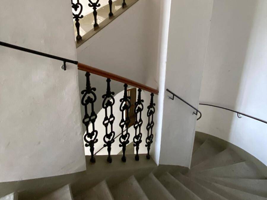 Historisches Treppenhaus mit schmiedeeisernem Geländer, Holzhandlauf und Steinstufen in einem Altbau.