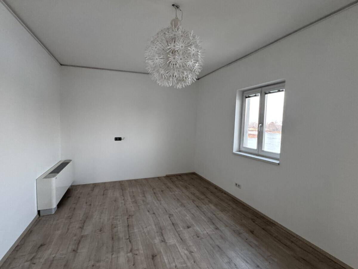 Heller, leerer Raum mit Laminatboden, weiß gestrichenen Wänden und einem modernen Deckenlicht.