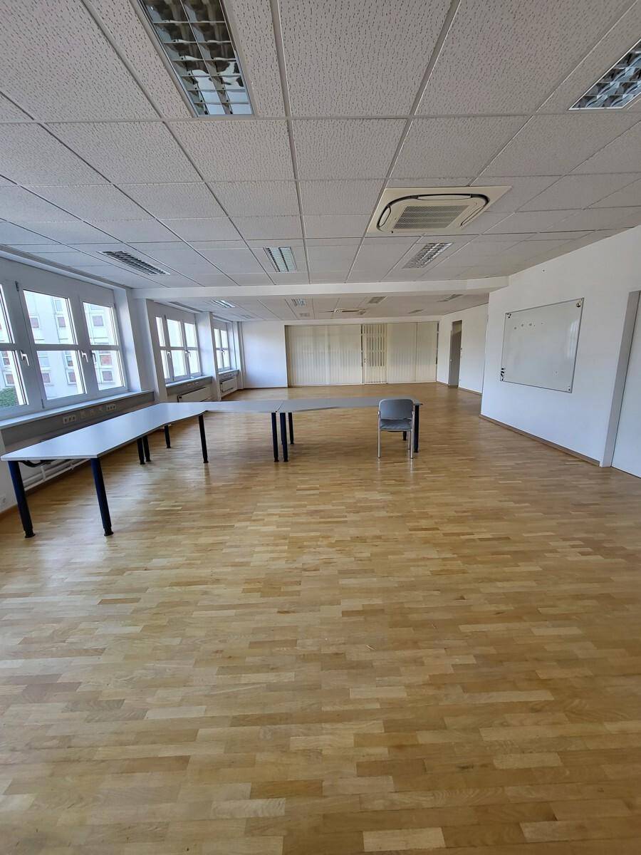 Geräumiges Büro mit hellem Holzparkett, großen Fenstern und Klimaanlage an der Decke.