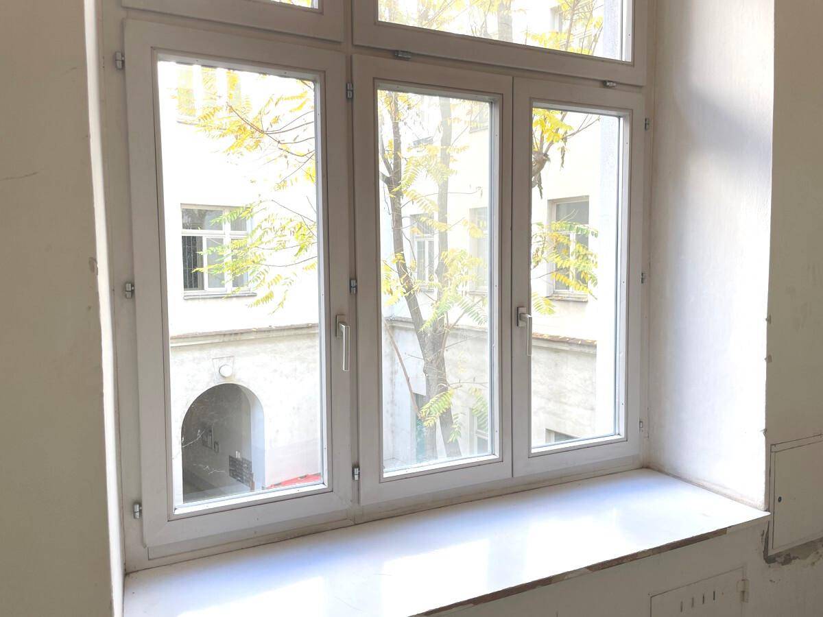 Großes Fenster mit Blick auf den grünen Innenhof und den Baum im Herbstlaub.