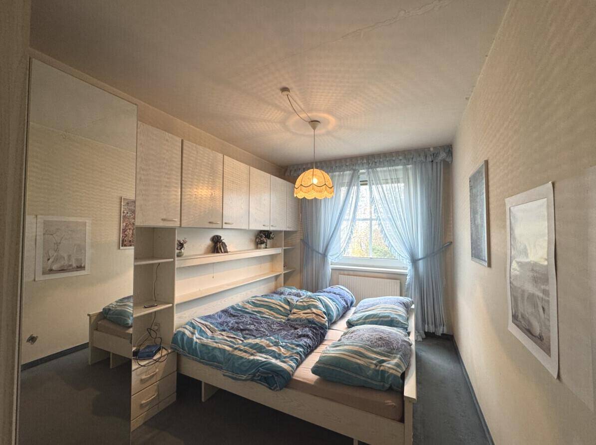 Schlafzimmer mit integrierten Schränken, einem Bett und einem Fenster mit Vorhängen.