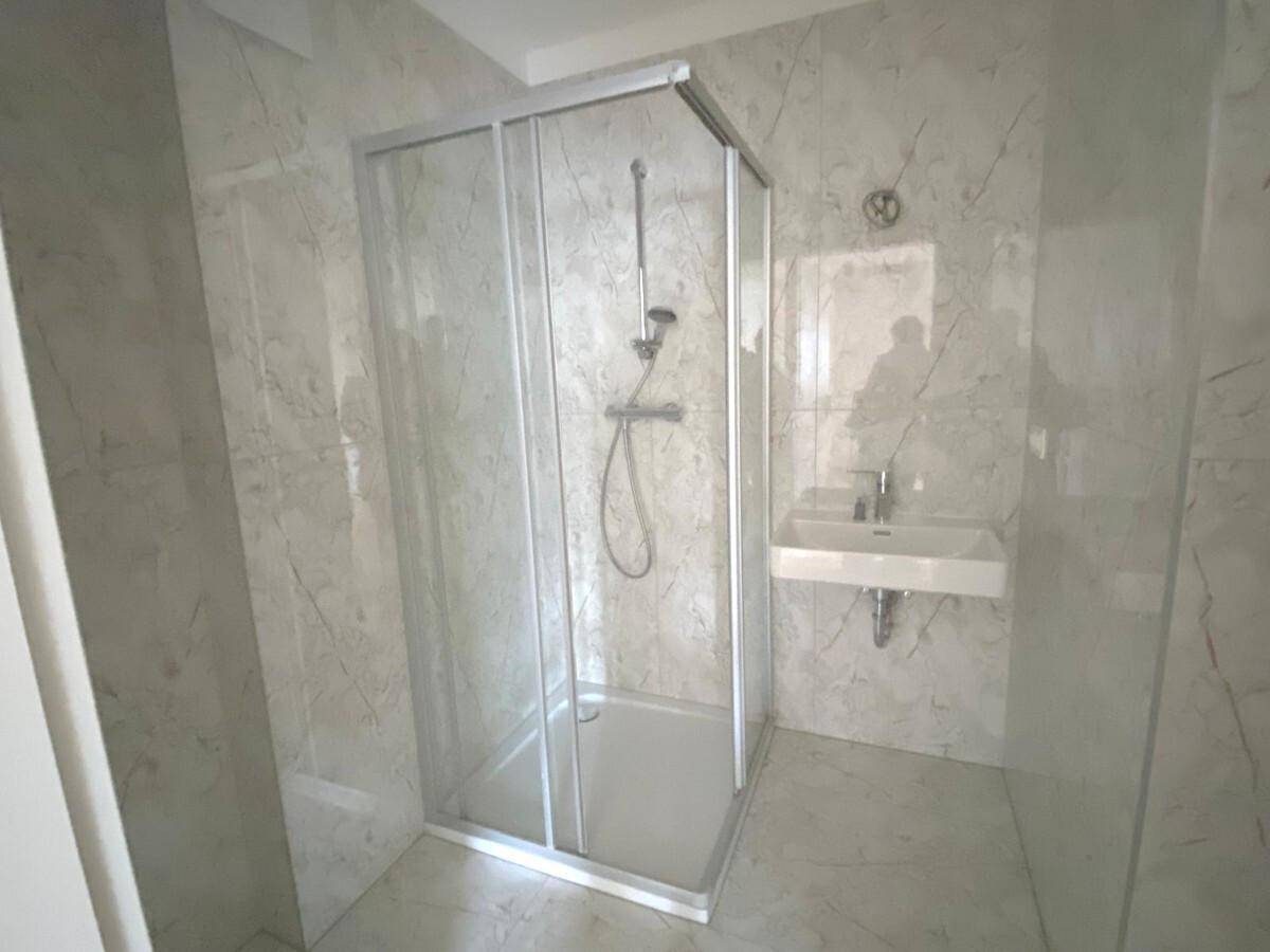 Modernes Badezimmer mit Duschkabine, wandmontiertem Waschbecken und hellen Marmorfliesen.