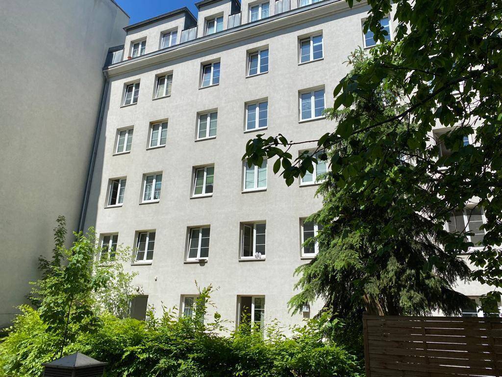 Mehrstöckiges Wohngebäude mit vielen Fenstern und einer hellen Fassade, umgeben von Bäumen.