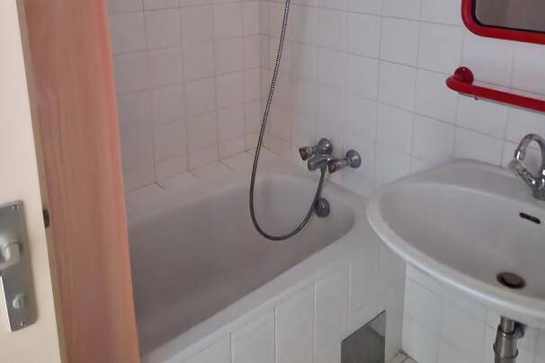 Kleines Badezimmer mit Badewanne, Waschbecken und weißen Fliesen, einfach und funktional ausgestattet.
