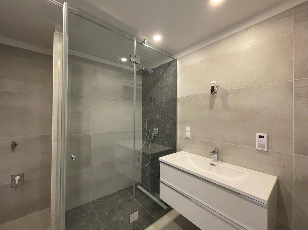Modernes Badezimmer mit begehbarer Dusche, großformatigen Fliesen und Einzelwaschbecken.