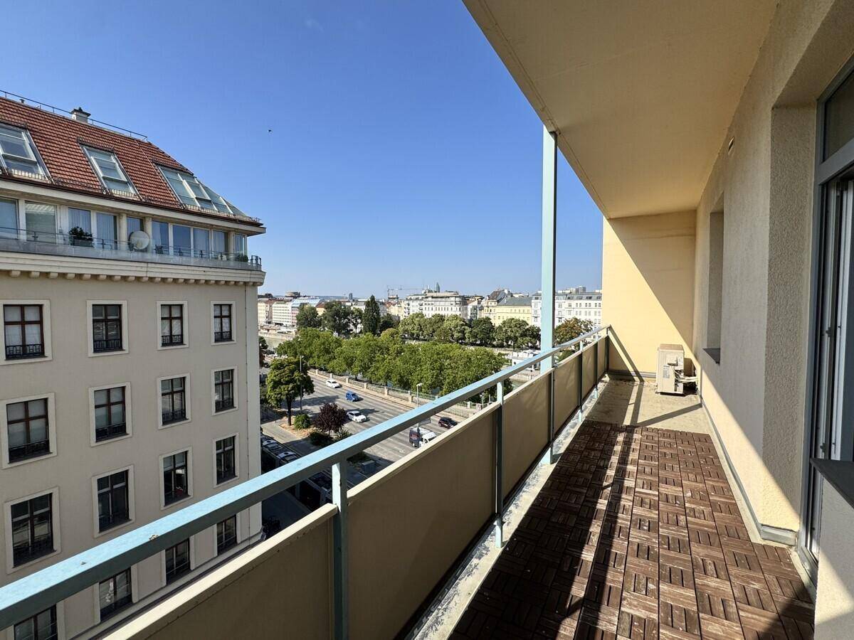 Langer Balkon mit Holzdielen und Blick auf die Straße und umliegende Gebäude.