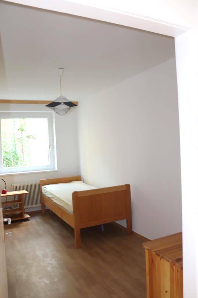 Helles Schlafzimmer mit Einzelbett, Holzboden und einem Fenster für viel Tageslicht.