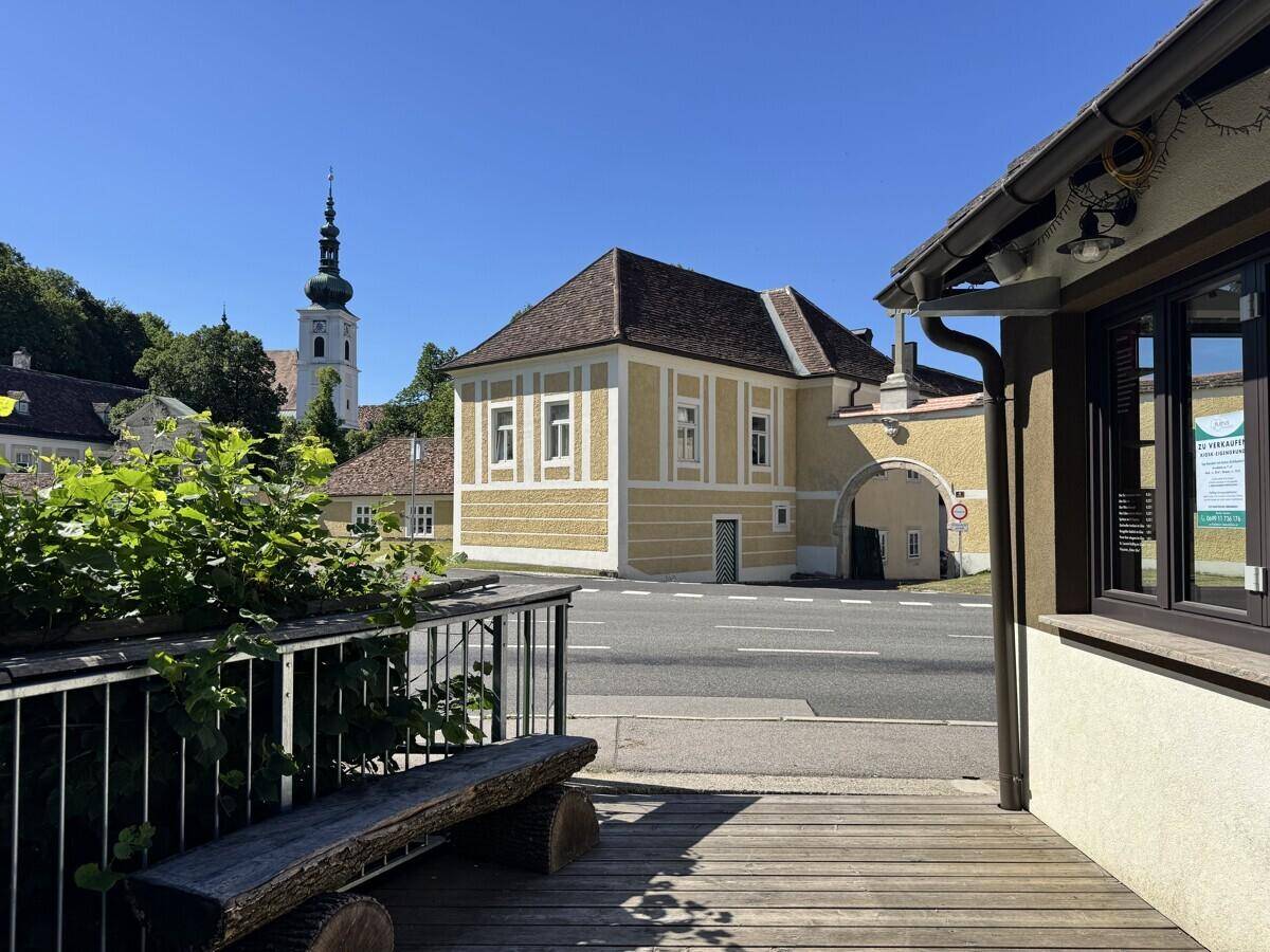 Holzterrasse mit Sitzbank und Blick auf historische Gebäude und eine Kirche im Hintergrund.