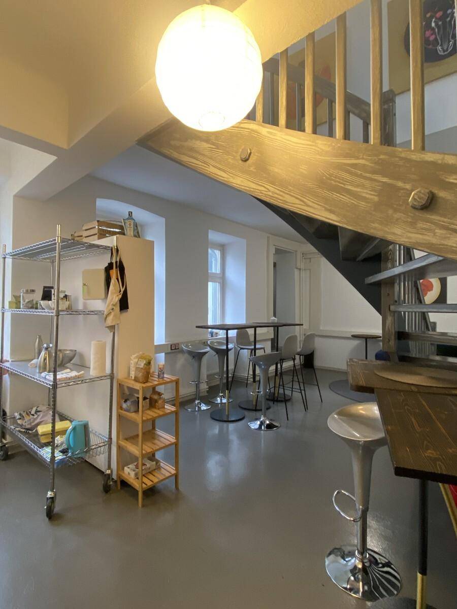 Offener Lounge-Bereich mit Barhockern, Regalen und einer markanten Holztreppe, ideal für gesellige Treffen.