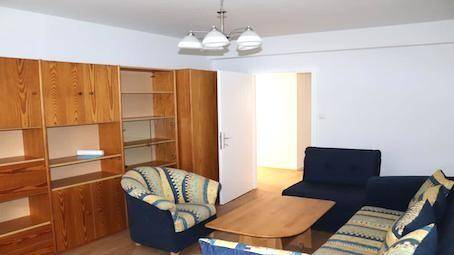 Wohnzimmer mit großer Holzschrankwand, blauen Sofas und gemustertem Sessel, gemütlich eingerichtet.