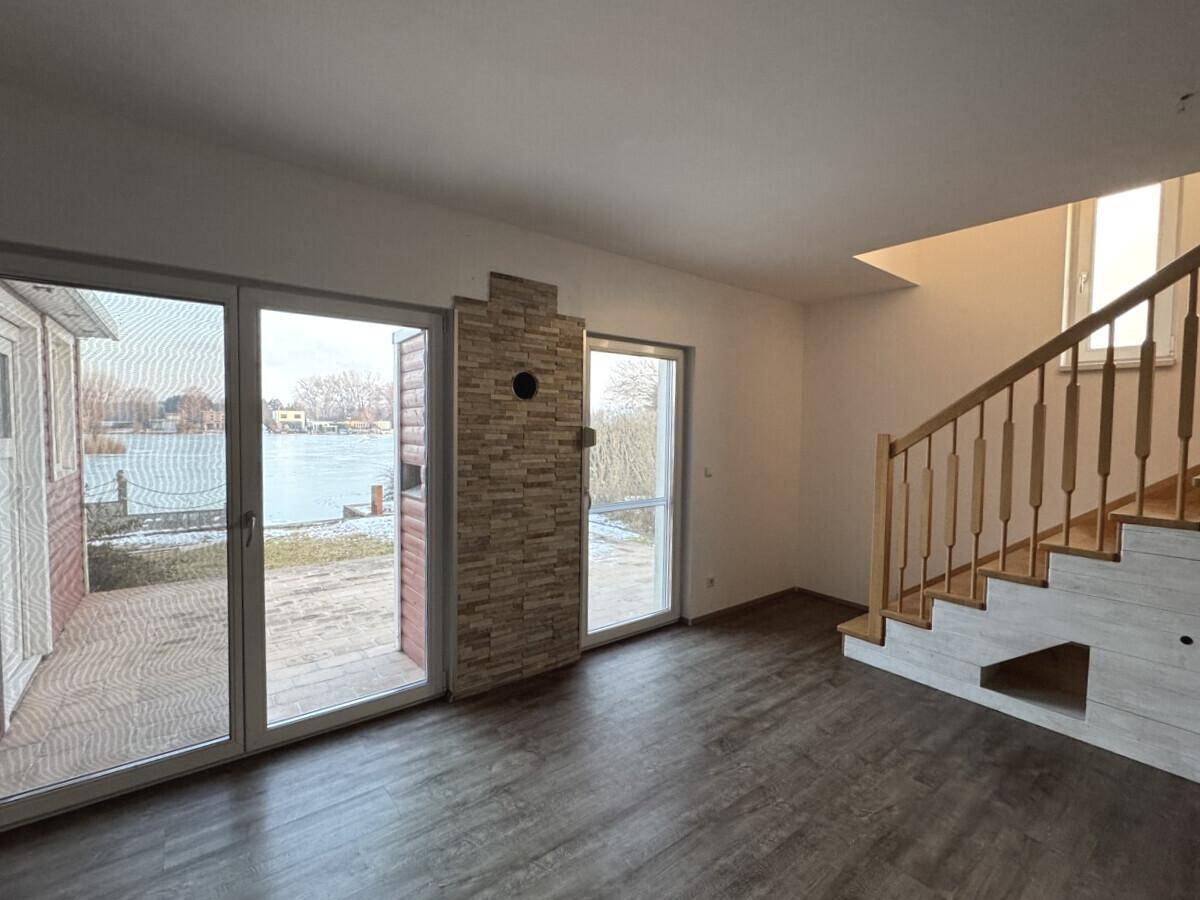 Heller Wohnbereich mit Seeblick, Holztreppe und modernem Steinakzent an der Wand.