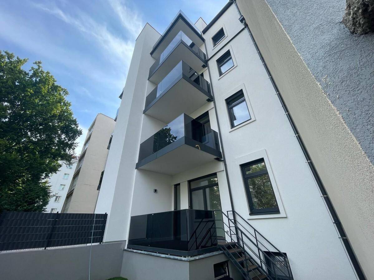 Moderne Gebäudefassade mit mehreren Balkonen und Glasbrüstungen unter blauem Himmel.