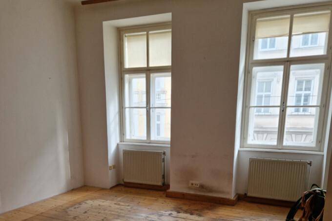 Zimmer mit Dielenboden und zwei Fenstern, die viel Tageslicht hereinlassen, ideal für eine Renovierung.